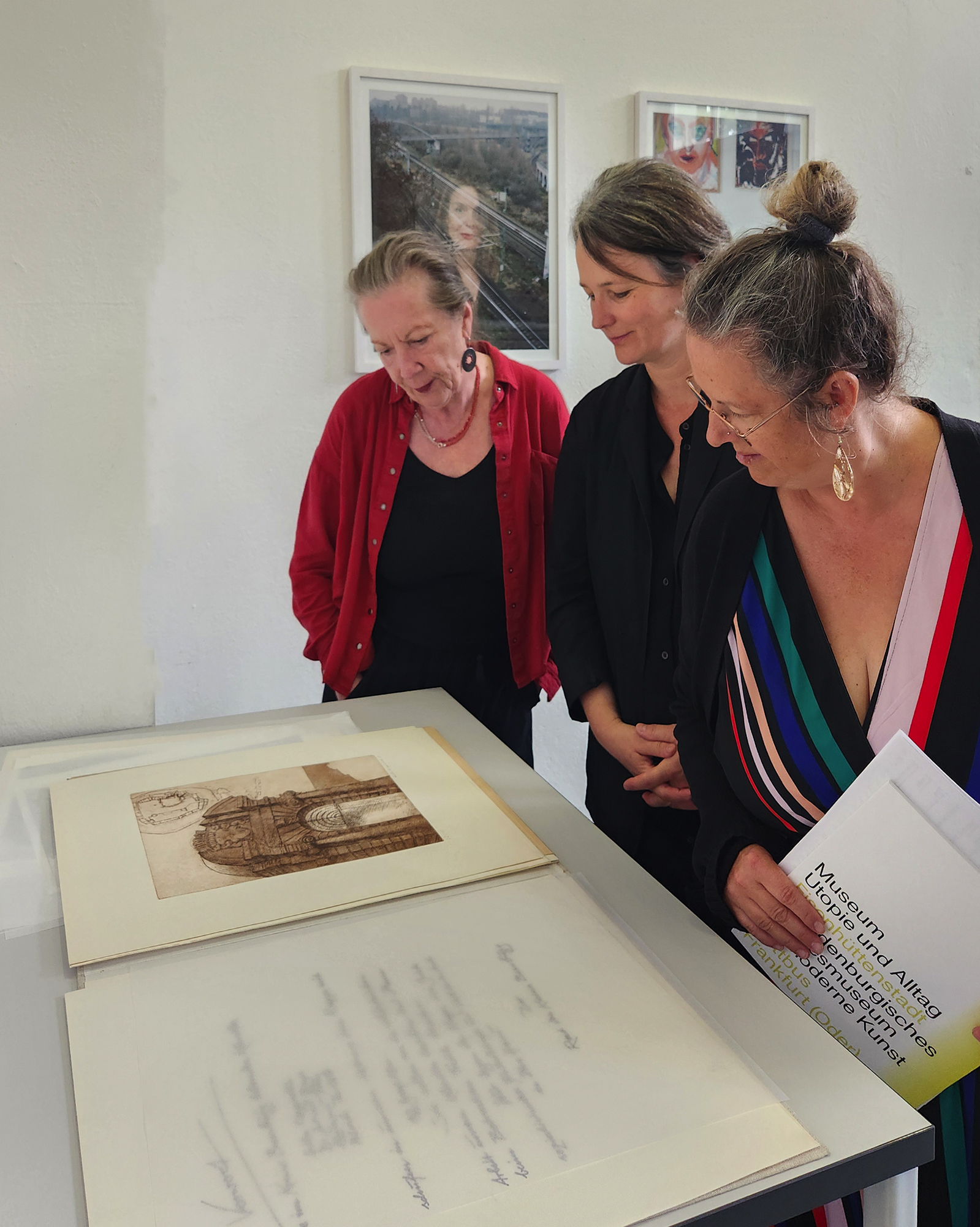 v.l. Jutta Jahn, Dr. Angelika Weißbach, Katja Reindel stehen gemeinsam vor einem Tisch und betrachten ein grafisches Kunstwerk.
